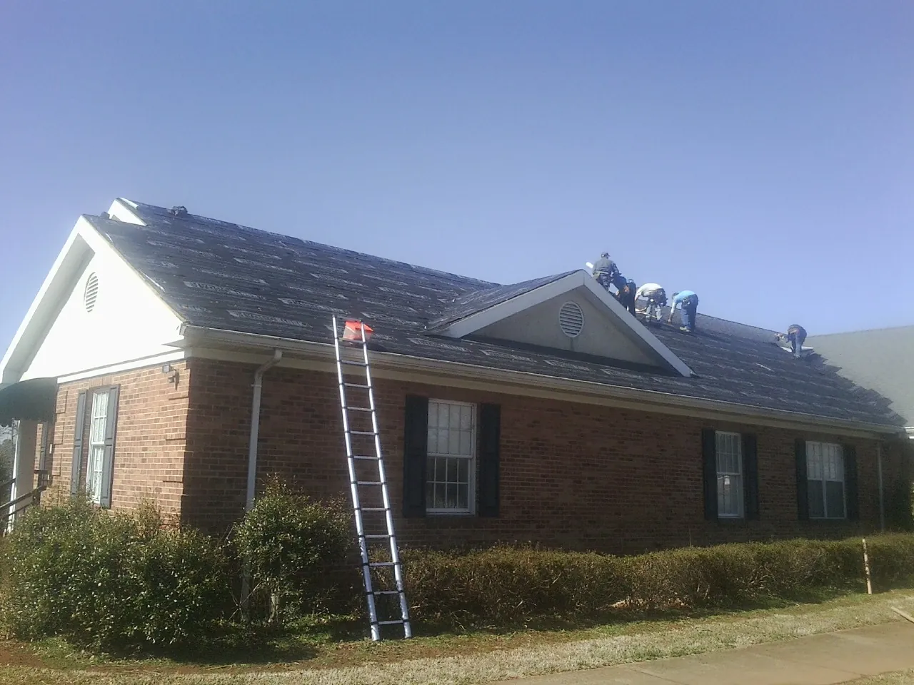 Crew tearing shingles off a brick ranch roof with a ladder set — Emergency Roof Repair work by our crew in Huntington Beach