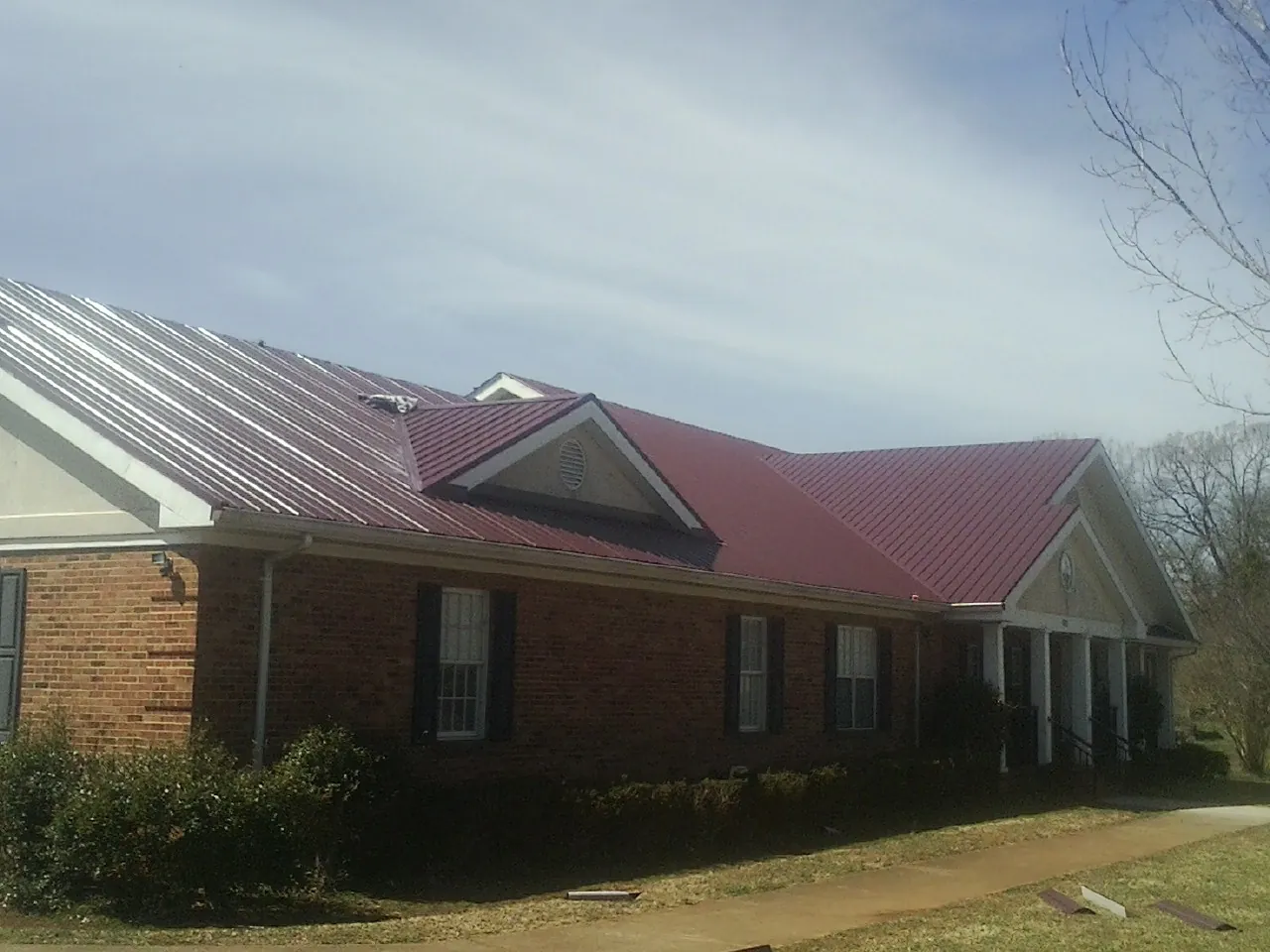 Red metal roof with gabled entries on a long brick building, from a Hail Damage Roof Repair job in Huntington Beach