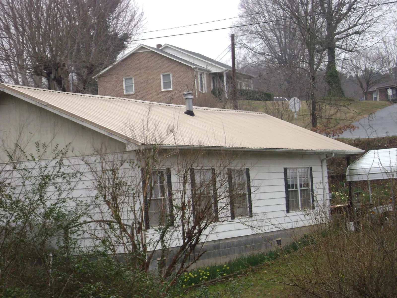 Tan metal roof on a white sided house set into a hillside — Commercial Roofing by Roofing Brothers in Huntington Beach